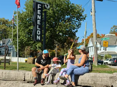 family sitting on the rocks by the water with the Fenelon sign in the background