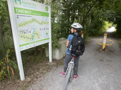 Lady on a bike looking at the Omemee Kawartha Trans Canada Trail sign