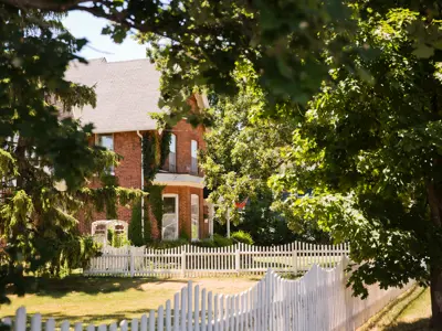View of house with white fence and green trees