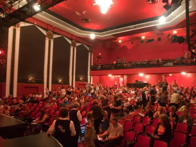 Inside the academy theatre, the audience is filling up the seats before a performance